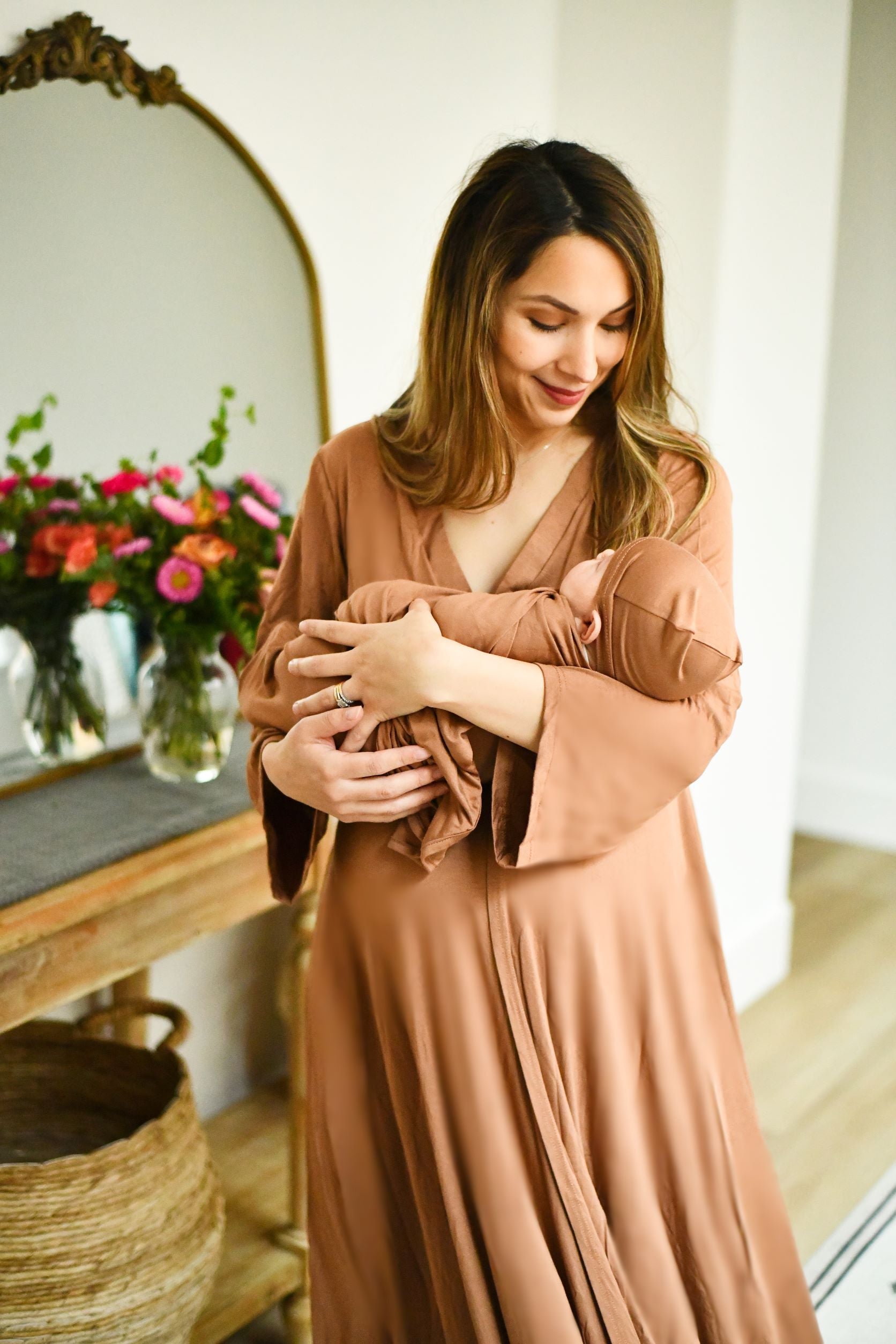 Mom wearing Lila caramel maternity labor birth gown holding baby in matching swaddle set with hat 